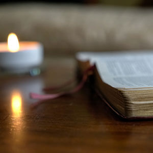 Open Bible With Burning Candle On The Table